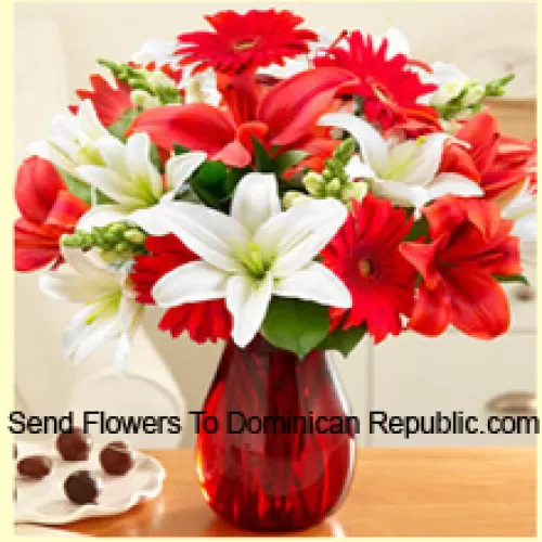 جيربيرا حمراء، زنابق بيضاء، زنابق حمراء وزهور متنوعة أخرى مرتبة بشكل جميل في مزهرية زجاجية